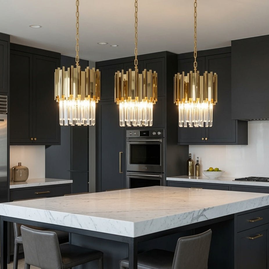 Three modern cylindrical pendant lights with gold-toned rods and clear glass shades hang over a white marble kitchen island in a contemporary dark gray kitchen.