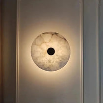 Witney sconce with glowing marble shade on a brass arm