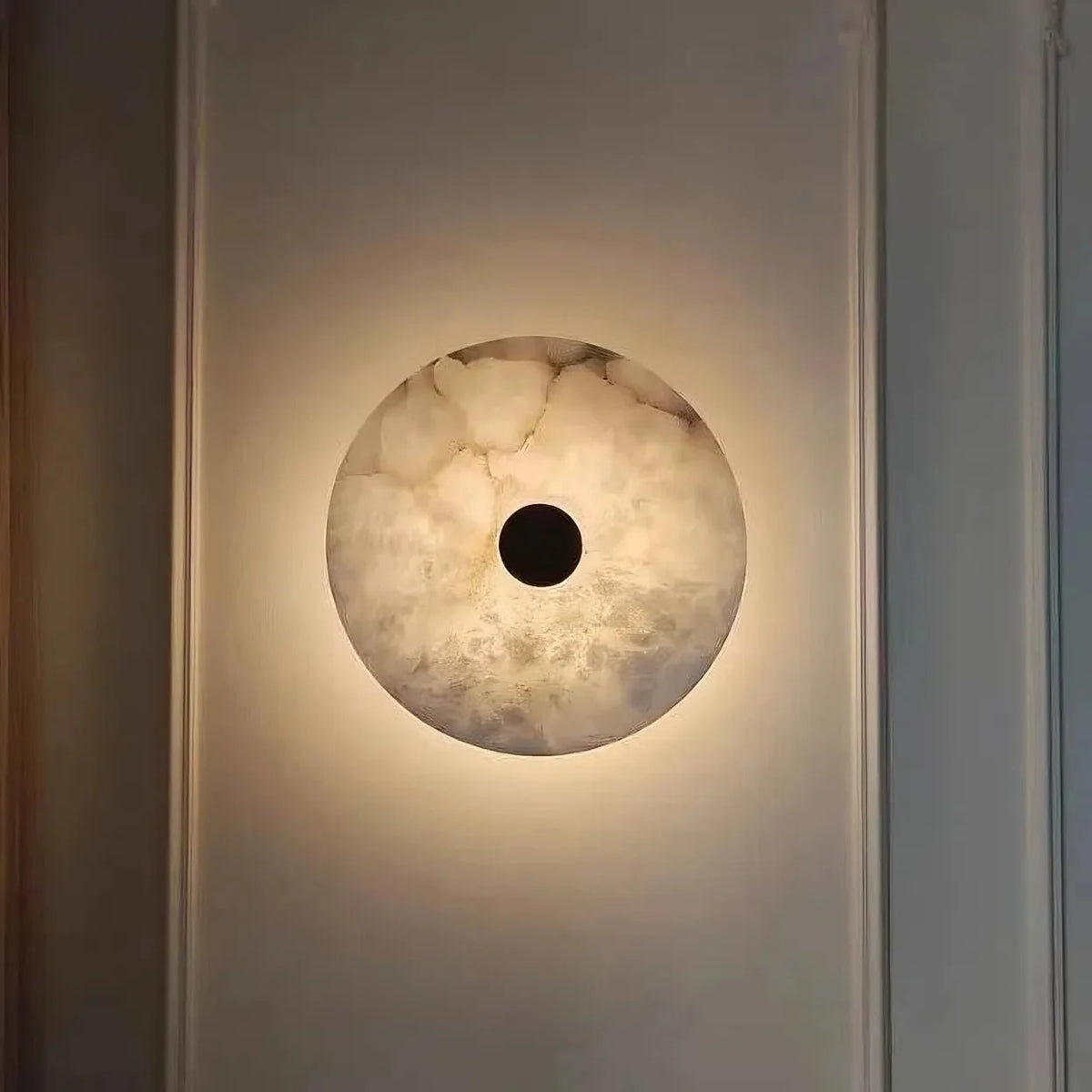Witney sconce with glowing marble shade on a brass arm